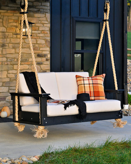 Outdoor swing with cushions on a porch, stone wall, and garden in the background